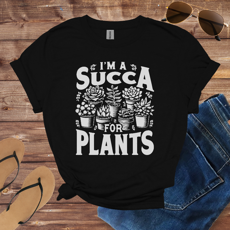 Black t-shirt with 'I'm a Succa for Plants' design on a wooden surface with sunglasses and jeans.