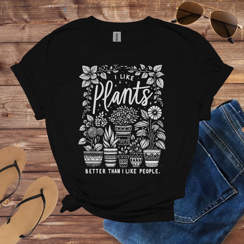 Black t-shirt with plant-themed design on a wooden surface with sunglasses and sandals.