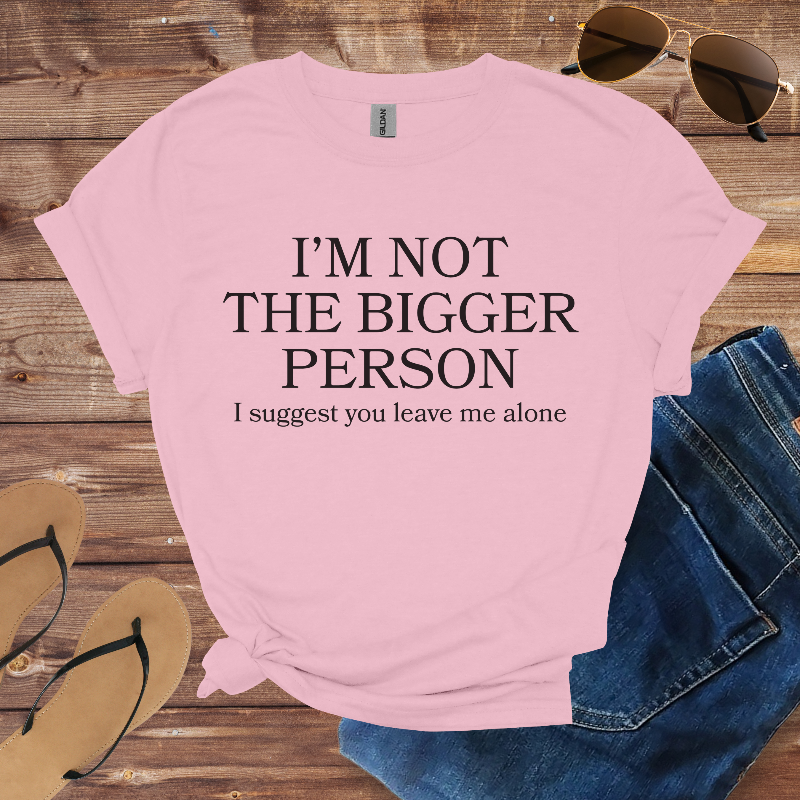 Pink t-shirt with humorous text on a wooden surface with sunglasses and jeans.