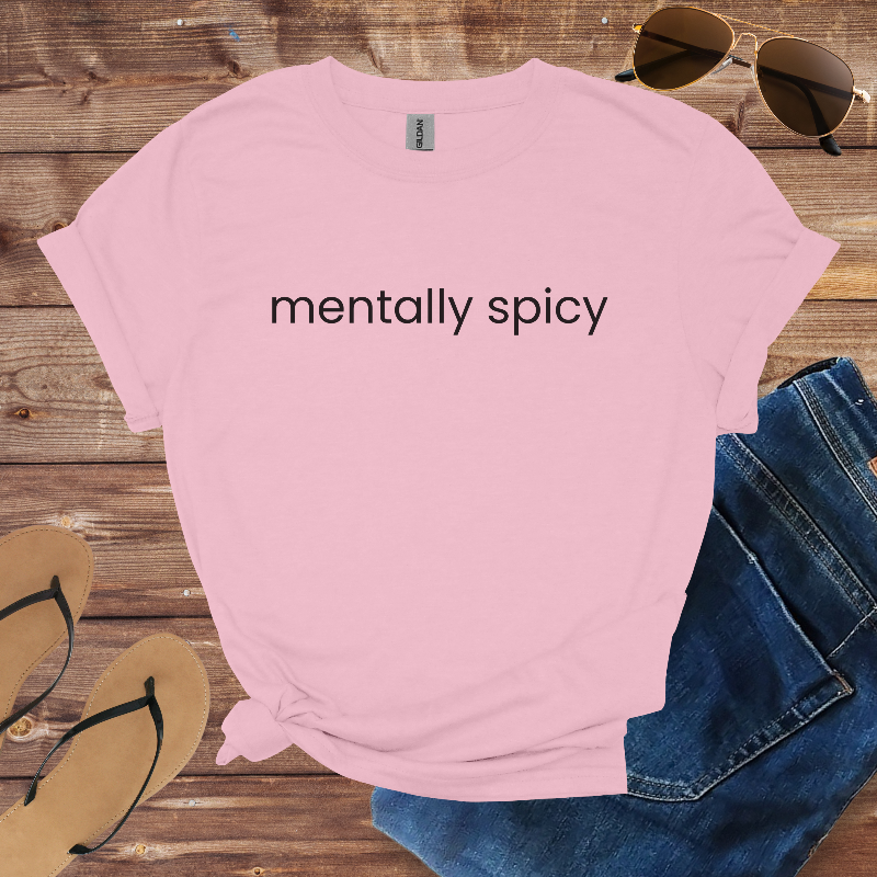 Pink t-shirt with 'mentally spicy' text on a wooden surface with sunglasses, jeans, and flip-flops.