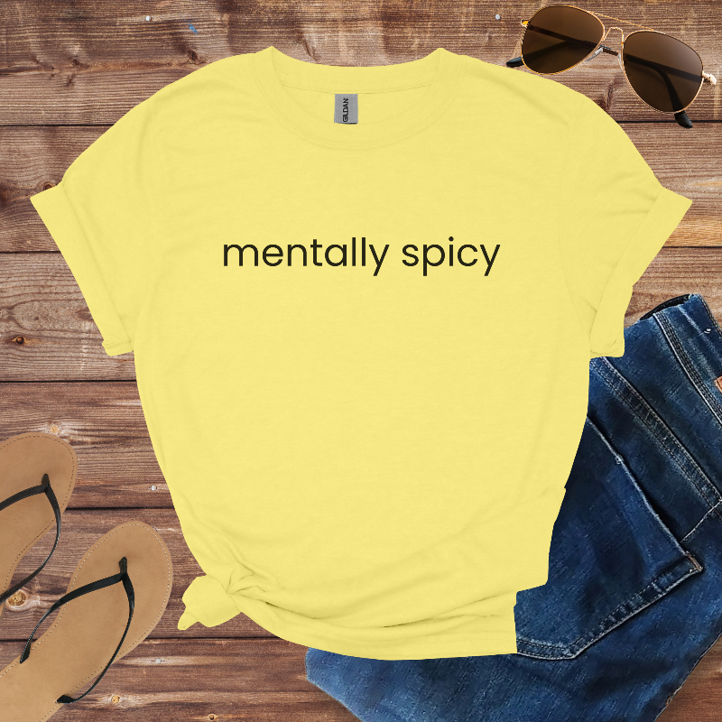 Yellow t-shirt with 'mentally spicy' text on a wooden surface with sunglasses, jeans, and sandals.