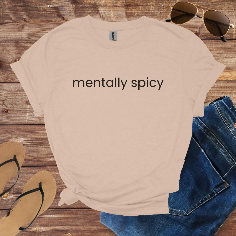 Beige t-shirt with 'mentally spicy' text on a wooden surface with sunglasses, jeans, and flip-flops.