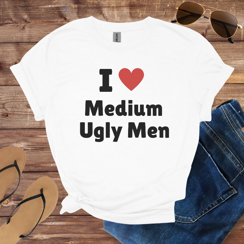 White t-shirt with 'I ❤️ Medium Ugly Men' text on a wooden surface with sunglasses, jeans, and sandals.