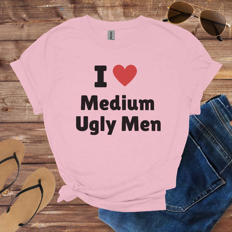 Pink t-shirt with text 'I ❤️ Medium Ugly Men' on a wooden surface with sunglasses, jeans, and sandals.