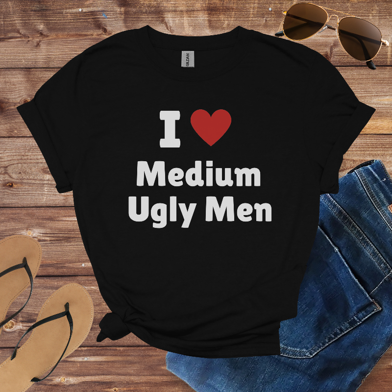 Black t-shirt with 'I ❤️ Medium Ugly Men' text on a wooden surface with sunglasses, jeans, and flip-flops.