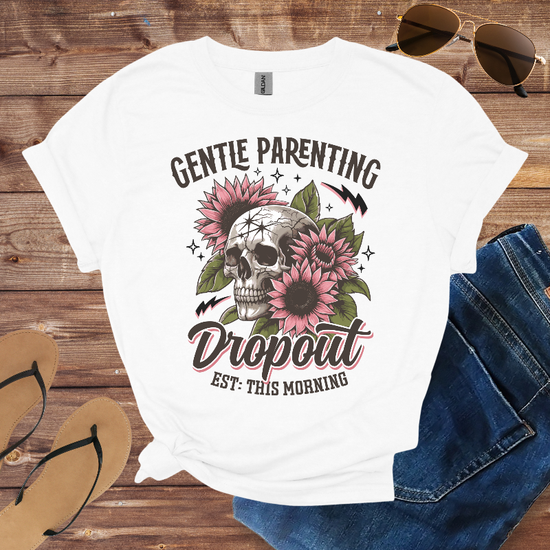 White t-shirt with skull and floral design on a wooden surface with sunglasses, jeans, and sandals.