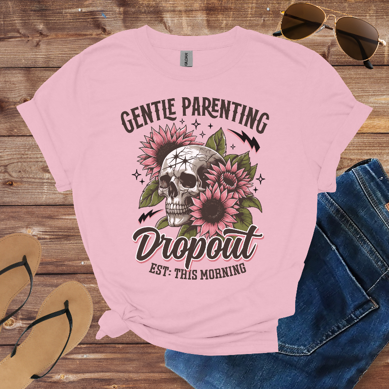 Pink t-shirt with skull and floral design on a wooden surface with sunglasses, jeans, and sandals.
