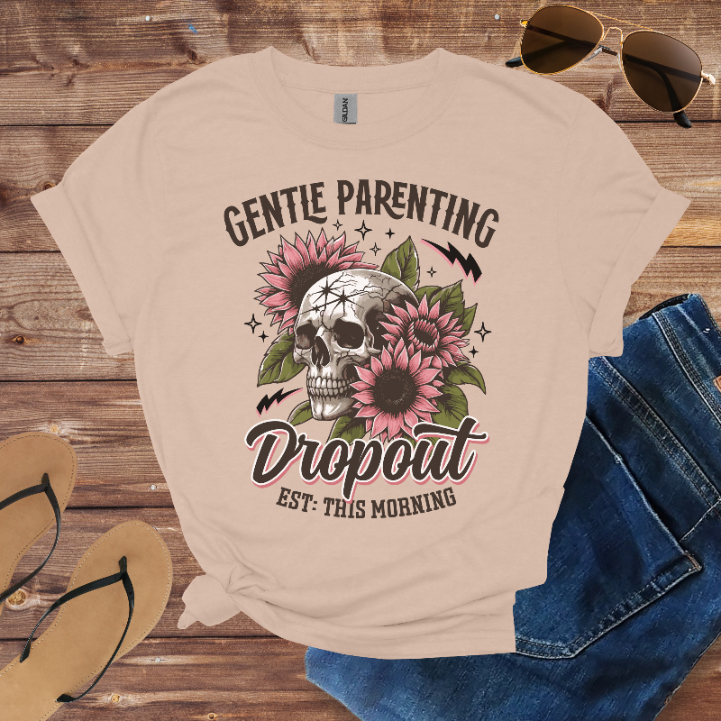 Beige t-shirt with skull and floral design on a wooden surface with sunglasses, jeans, and sandals.