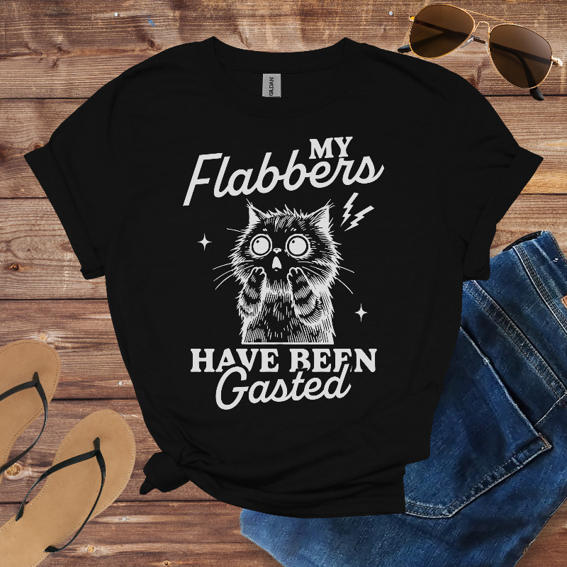 Black t-shirt with a graphic of a cat and text on a wooden surface with sunglasses and sandals.