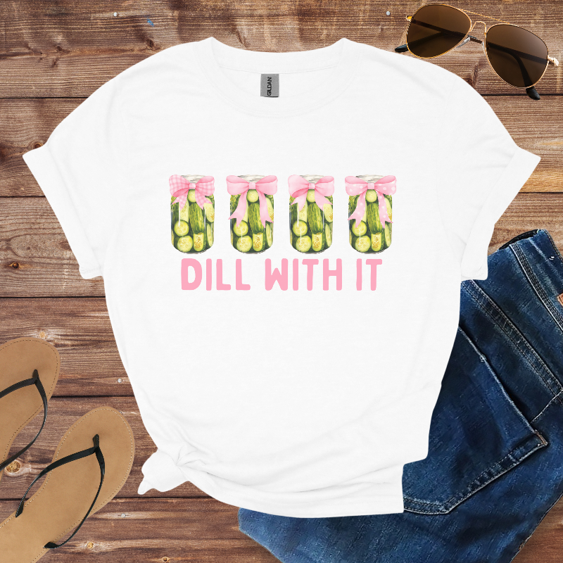 White t-shirt with 'Dill With It' graphic on a wooden surface with sunglasses, jeans, and sandals.