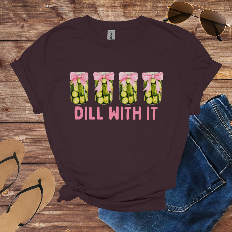 Brown t-shirt with 'Dill With It' graphic on a wooden surface with sunglasses, jeans, and sandals.