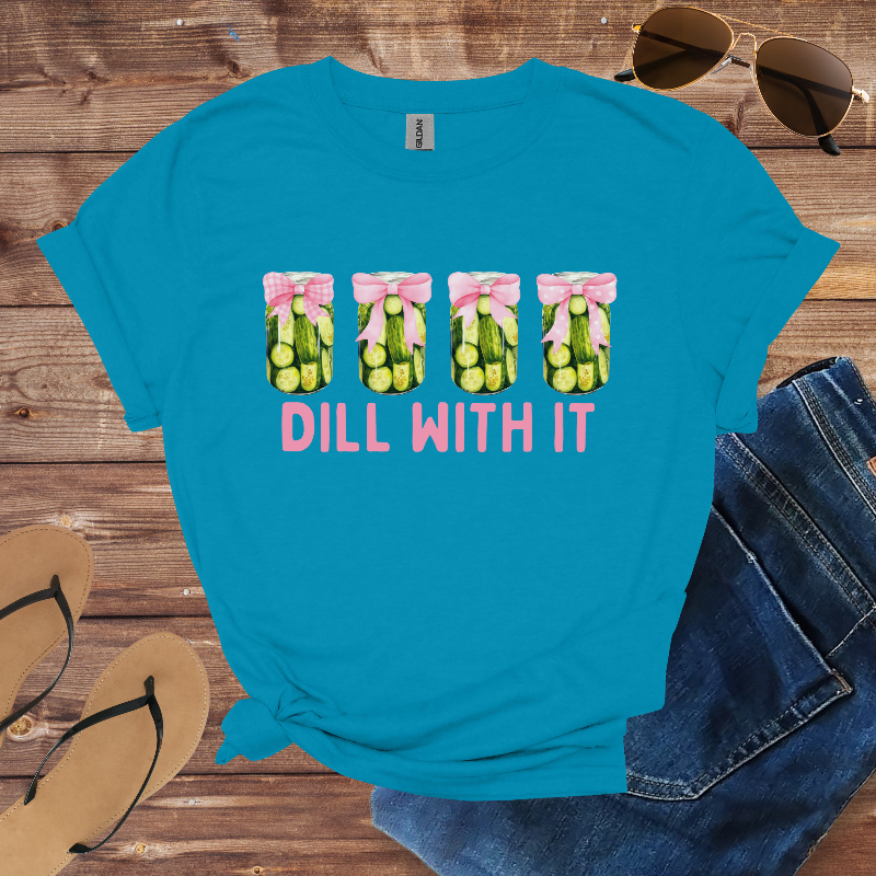 Blue t-shirt with 'Dill With It' graphic on a wooden surface with sunglasses, jeans, and sandals.