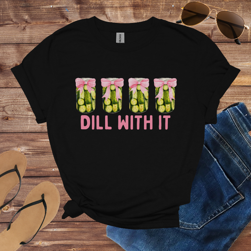 Black t-shirt with 'Dill With It' graphic on a wooden surface with sunglasses, jeans, and sandals.