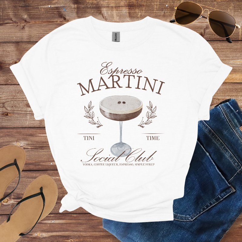 White t-shirt with 'Espresso Martini' design on a wooden surface with sunglasses, jeans, and flip-flops.