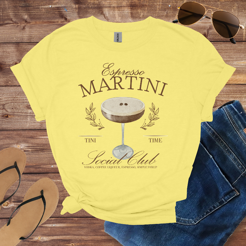 Yellow t-shirt with 'Espresso Martini' design on a wooden surface with sunglasses, jeans, and flip-flops.