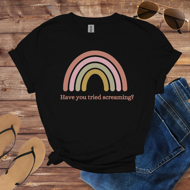 Black t-shirt with a rainbow graphic and text on a wooden surface with sunglasses and jeans.