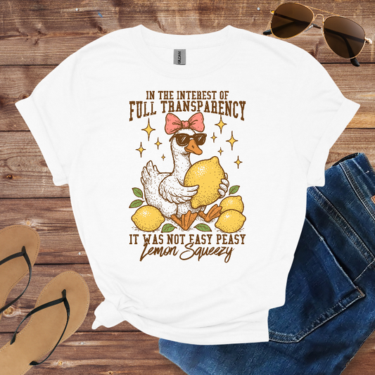 White t-shirt with a graphic of a duck holding lemons and text on a wooden surface with sunglasses and flip-flops.