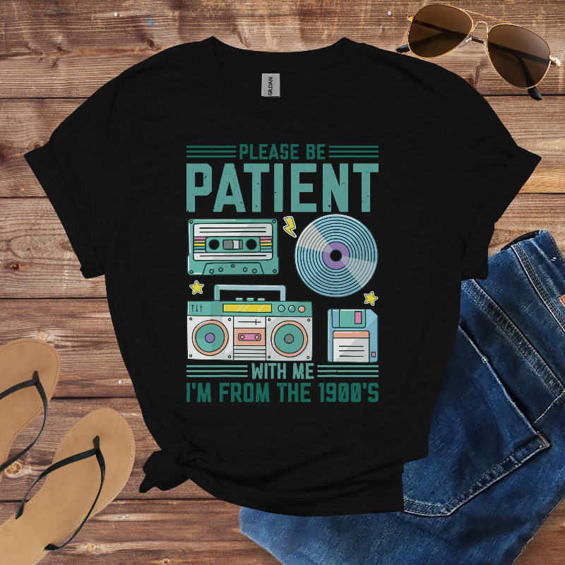 Black t-shirt with retro design and text on a wooden surface with sunglasses, jeans, and sandals.