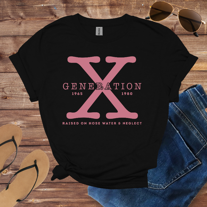 Black t-shirt with pink 'Generation X' design on a wooden surface with sunglasses, jeans, and flip-flops.