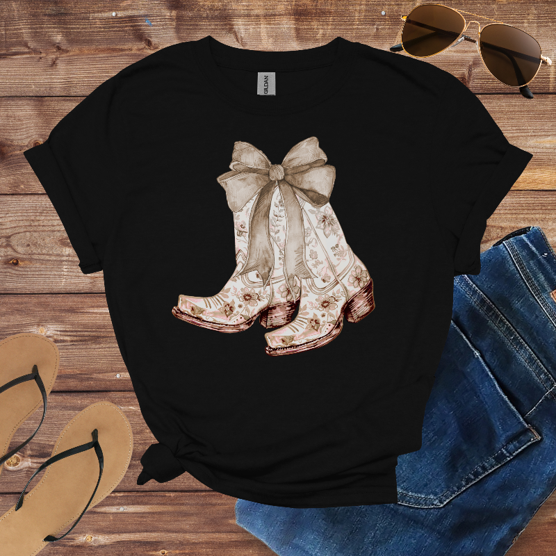 Black t-shirt with cowboy boot design on a wooden surface with sunglasses and jeans.