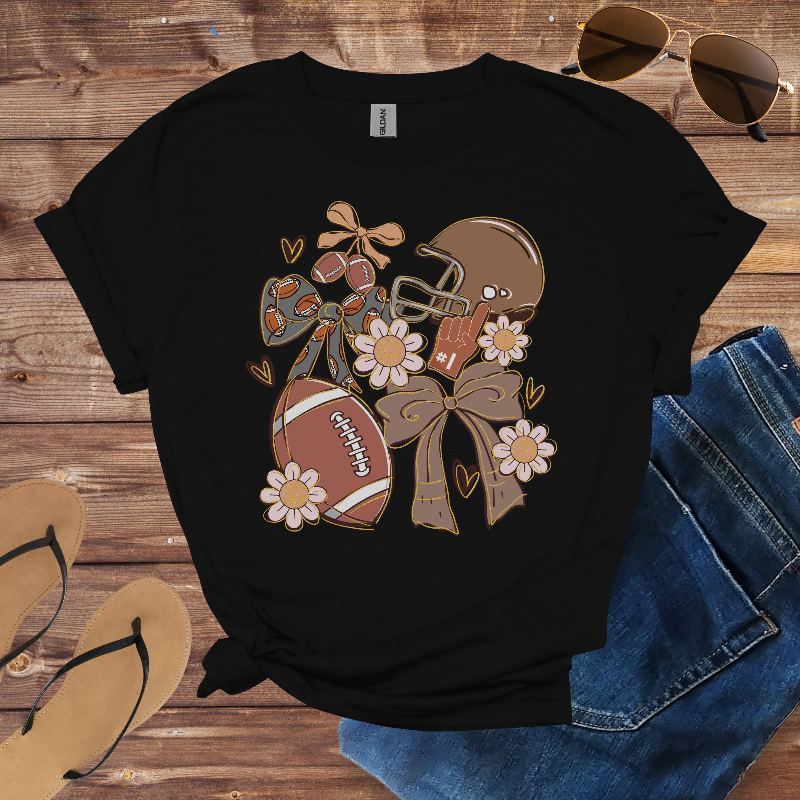 Black t-shirt with football, helmet, and flower design on a wooden surface with sunglasses and jeans.