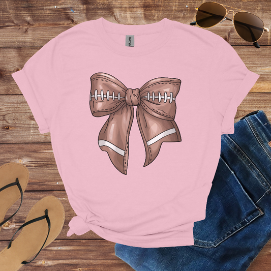 Pink t-shirt with a brown bow graphic on a wooden surface with sunglasses and jeans.