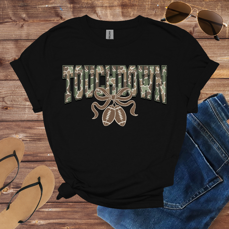 Black t-shirt with 'Touchdown' graphic on a wooden surface with sunglasses, jeans, and flip-flops.