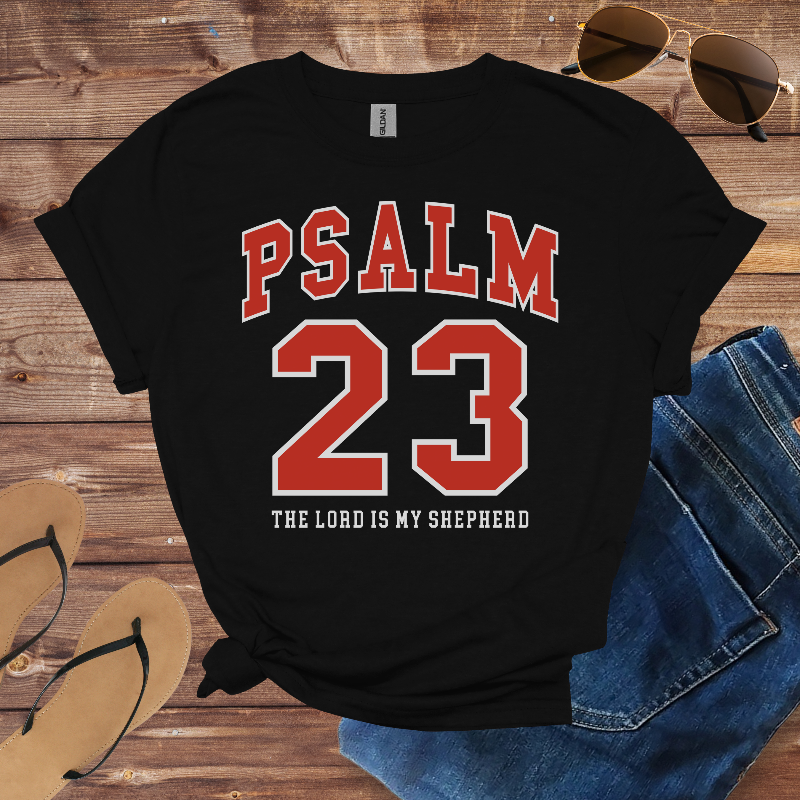 Black t-shirt with 'Psalm 23' design on a wooden surface with sunglasses and jeans.