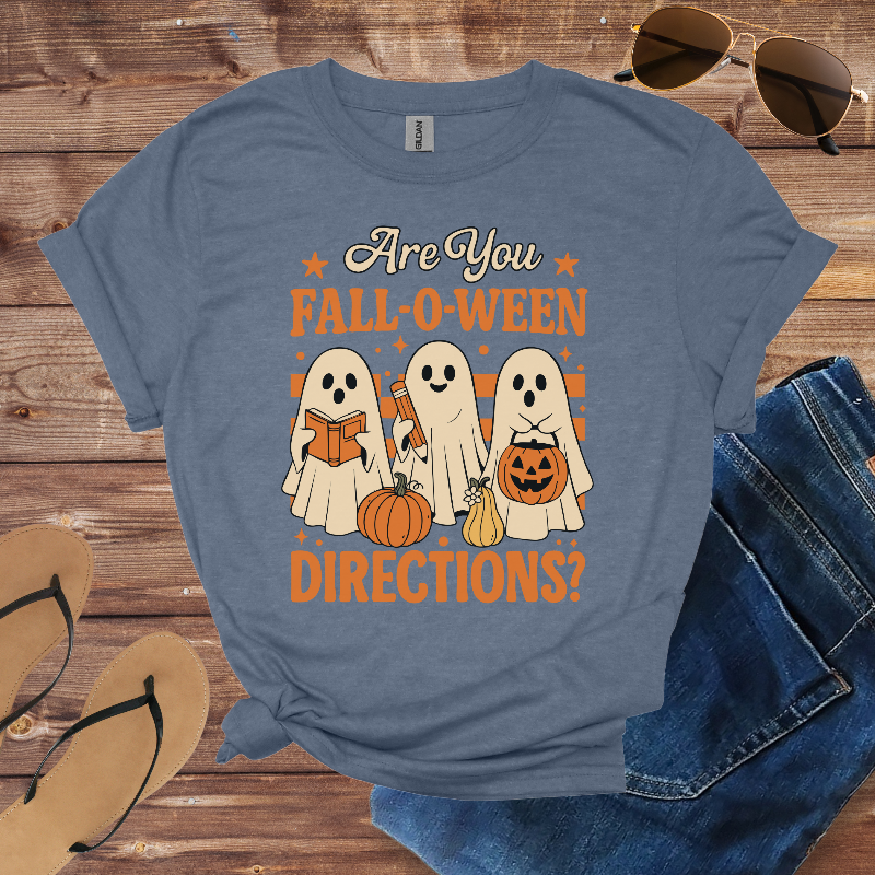 Blue t-shirt with Halloween design featuring ghosts and pumpkins on a wooden surface with sunglasses, jeans, and flip-flops.