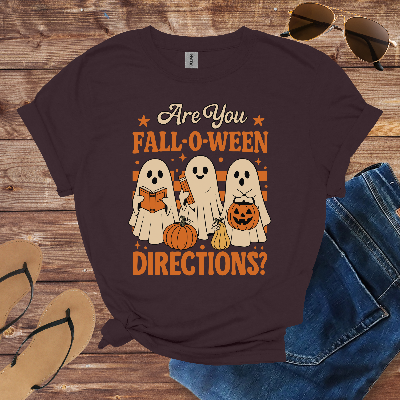 Halloween-themed t-shirt with ghosts and pumpkins on a wooden surface with sunglasses, jeans, and flip-flops.