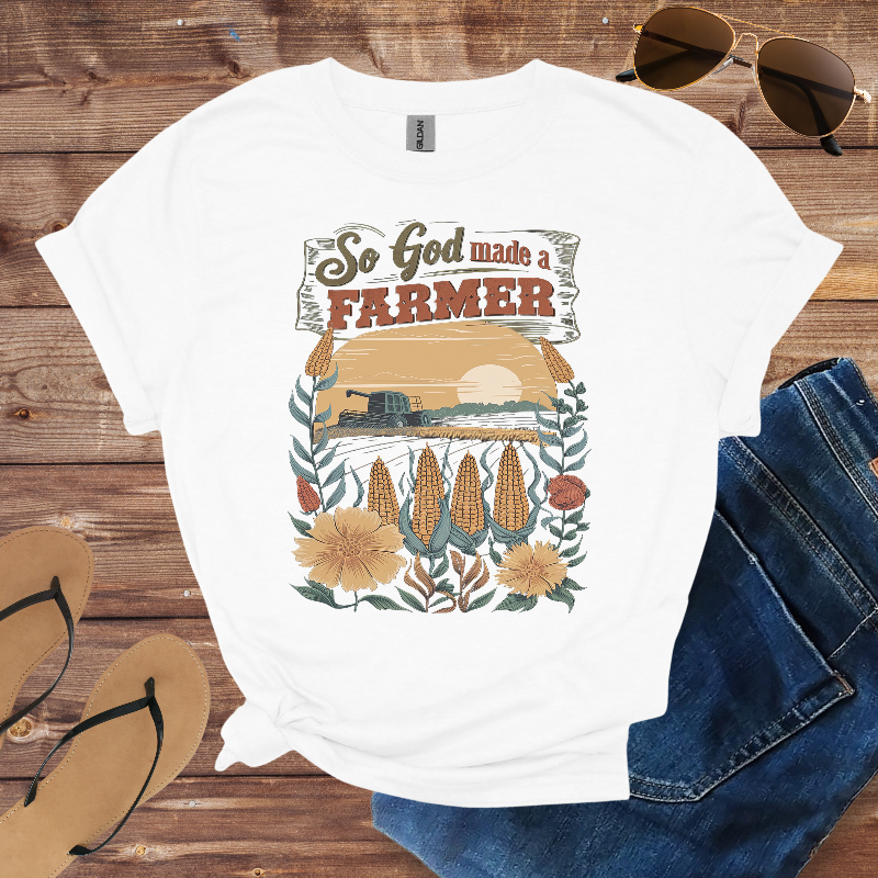 White t-shirt with farmer graphic design on a wooden surface with sunglasses, jeans, and sandals.