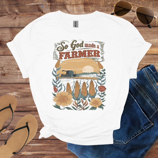 White t-shirt with farmer graphic design on a wooden surface with sunglasses, jeans, and sandals.