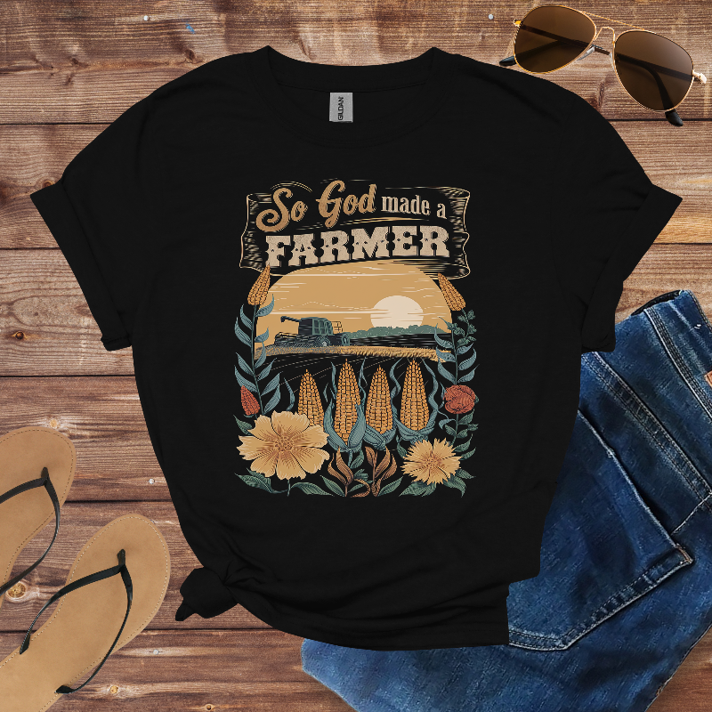 Black t-shirt with 'So God made a Farmer' graphic on a wooden surface with sunglasses, sandals, and jeans.