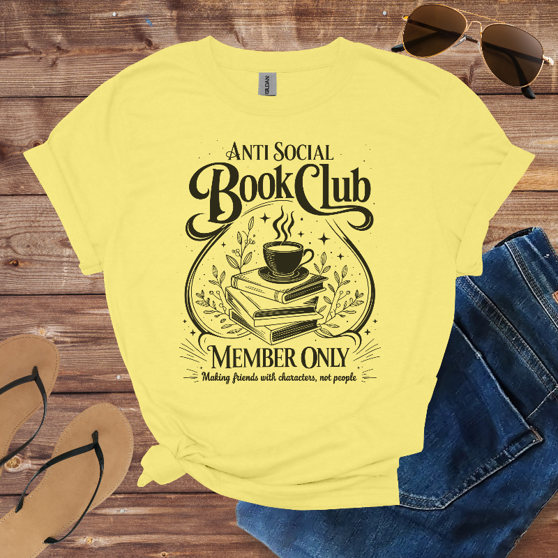 Yellow t-shirt with 'Anti Social Book Club' design on a wooden surface with sunglasses, jeans, and sandals.