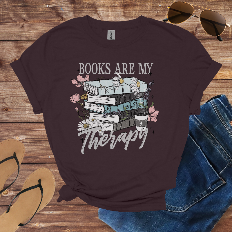 Brown t-shirt with 'Books are my Therapy' design on a wooden surface with sunglasses, jeans, and sandals.