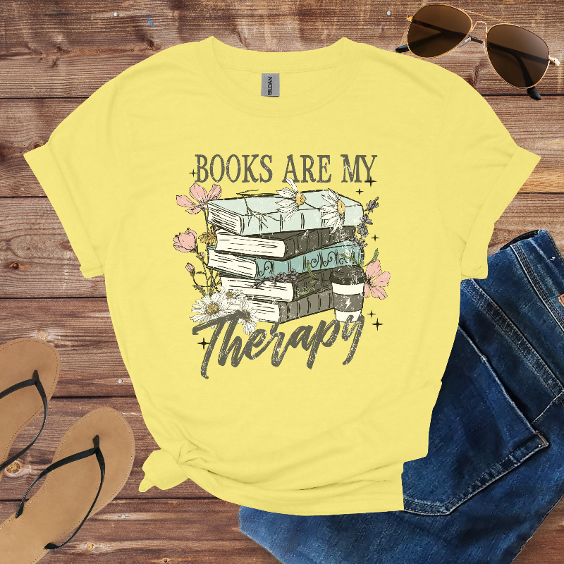Yellow t-shirt with 'Books are my Therapy' design on a wooden surface with sunglasses and jeans.