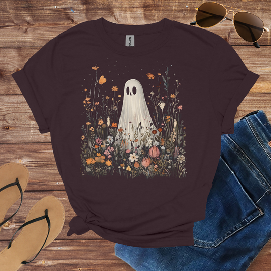 T-shirt with ghost and floral design on a wooden surface with sunglasses, jeans, and sandals.