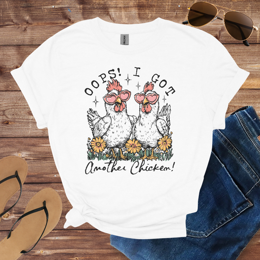 White t-shirt with chicken graphic and text on a wooden surface with sunglasses and sandals.