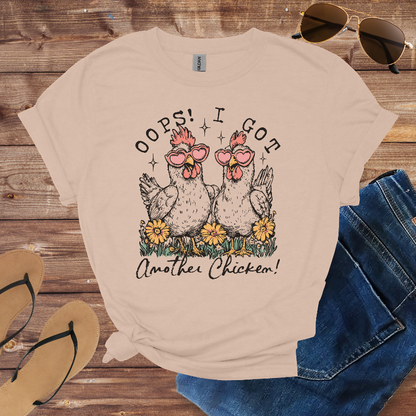 Beige t-shirt with chicken graphic and text on a wooden surface with sunglasses and jeans.