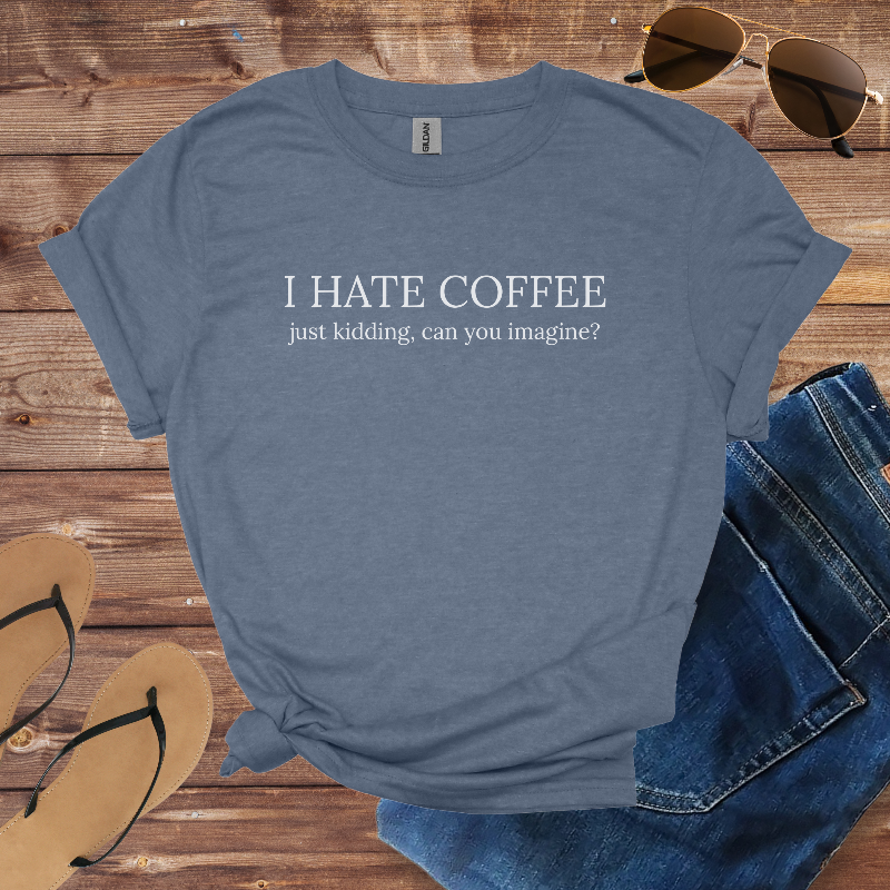 Blue t-shirt with 'I HATE COFFEE just kidding, can you imagine?' text on a wooden surface with sunglasses, jeans, and sandals.
